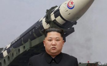leader stands before large missile with military vehicle in background