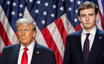 two men in suits with American flag backdrop, serious expressions