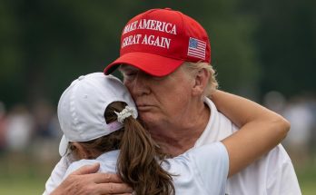 man in red cap embraces young golfer on green course
