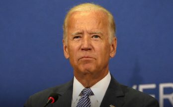 man in suit at podium during speech, blue background