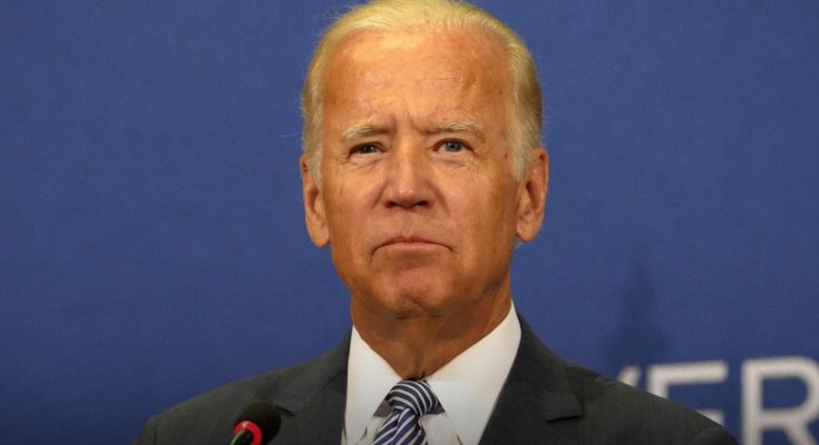 man in suit at podium during speech, blue background