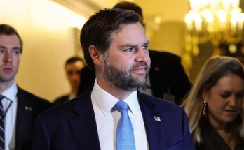 JD Vance walking through ornate hallway with staff, wearing navy suit and light blue tie