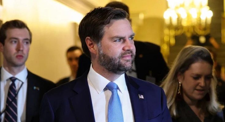 JD Vance walking through ornate hallway with staff, wearing navy suit and light blue tie