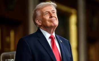 donald Trump in navy suit and red tie stands indoors with ornate columns behind him