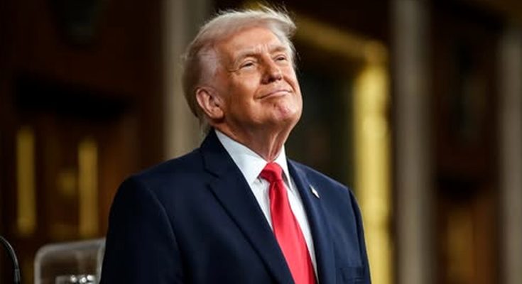 donald Trump in navy suit and red tie stands indoors with ornate columns behind him