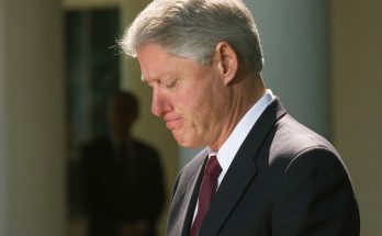 man in suit looking down, solemn expression, outdoor setting