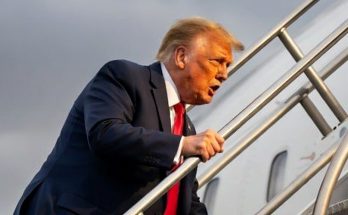 man in suit ascending airplane stairs under cloudy sky