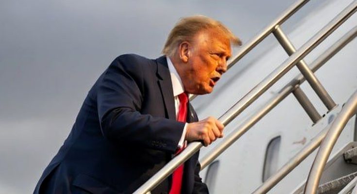 man in suit ascending airplane stairs under cloudy sky