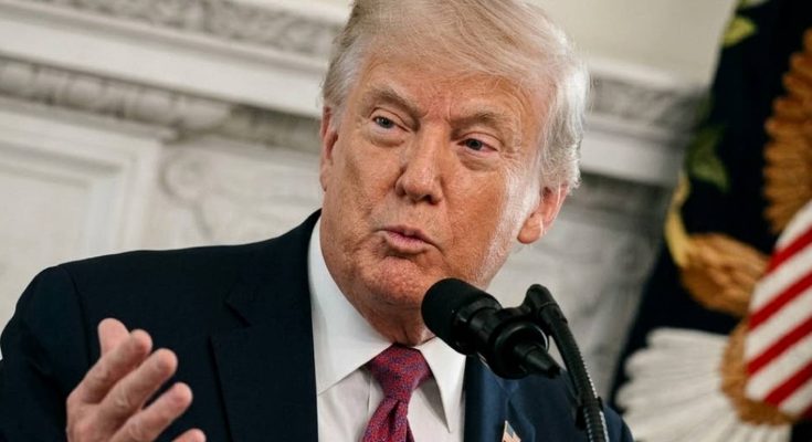 donald Trump speaking at podium with microphone, wearing dark suit and red patterned tie