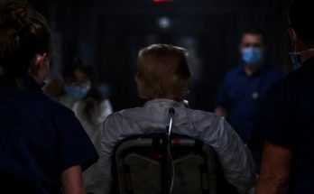 medical team in masks escorting patient in dark corridor