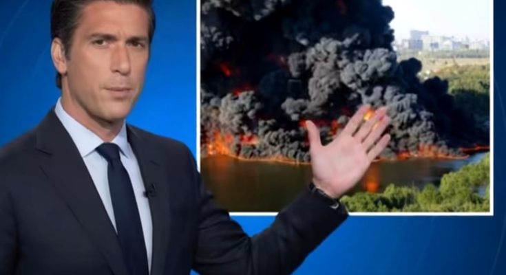 news anchor reports on massive fire with smoke cloud in background