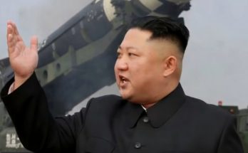 leader gestures beside large missile during military demonstration