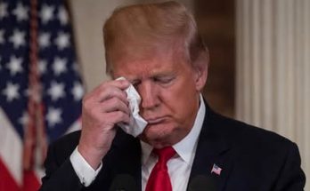 man wiping face with tissue, American flag in background