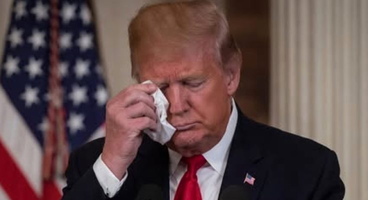 man wiping face with tissue, American flag in background