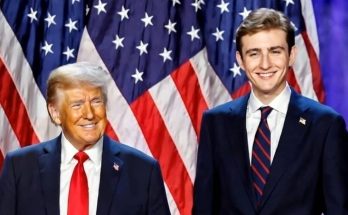 two men in suits stand smiling in front of American flags