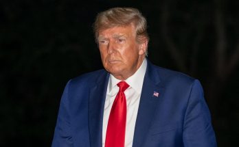 man in blue suit and red tie standing against a dark background