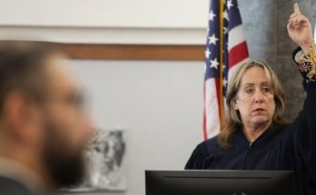 judge announces life sentence verdict in courtroom with flag