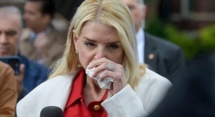 woman in red coat wiping nose amid crowd during press event