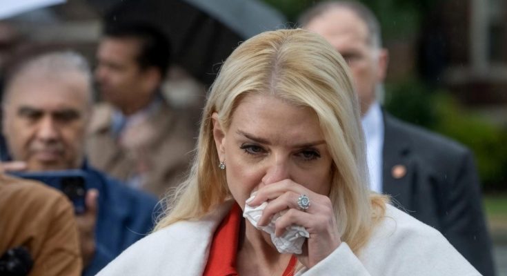 blonde woman in red coat speaks at outdoor press event