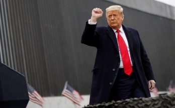 former leader gestures near border wall with flags and podium