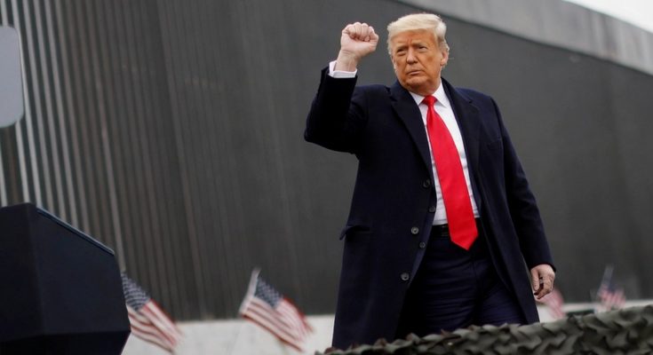 former leader gestures near border wall with flags and podium
