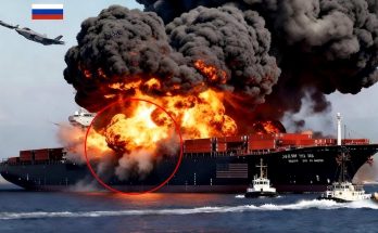 cargo ship engulfed in flames with military aircraft overhead