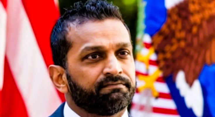 serious man stands before American flags outdoors
