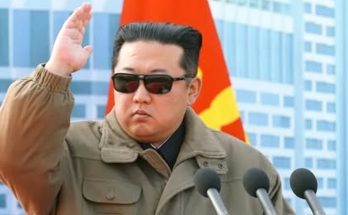 leader in sunglasses saluting at podium with microphones, flags behind