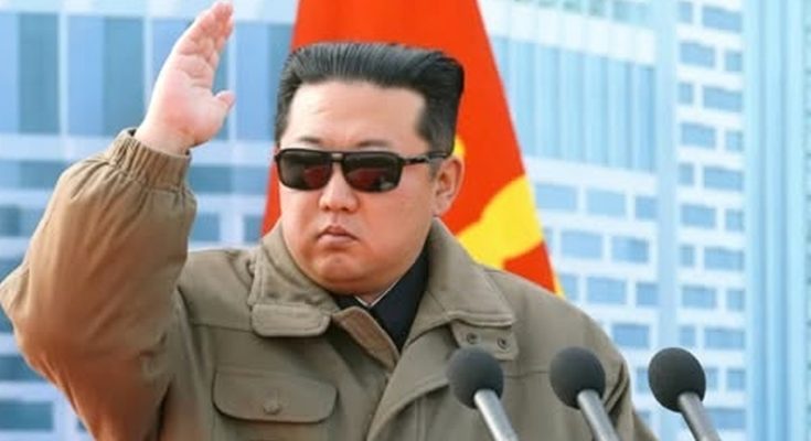 leader in sunglasses saluting at podium with microphones, flags behind