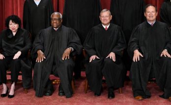 judges in black robes seated on wooden chairs, red backdrop