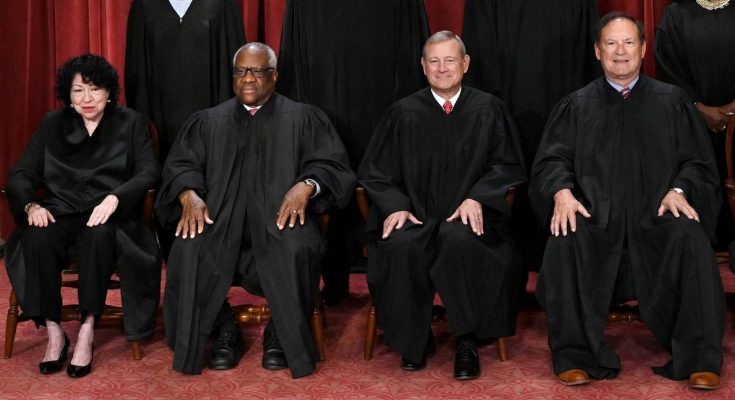 judges in black robes seated on wooden chairs, red backdrop